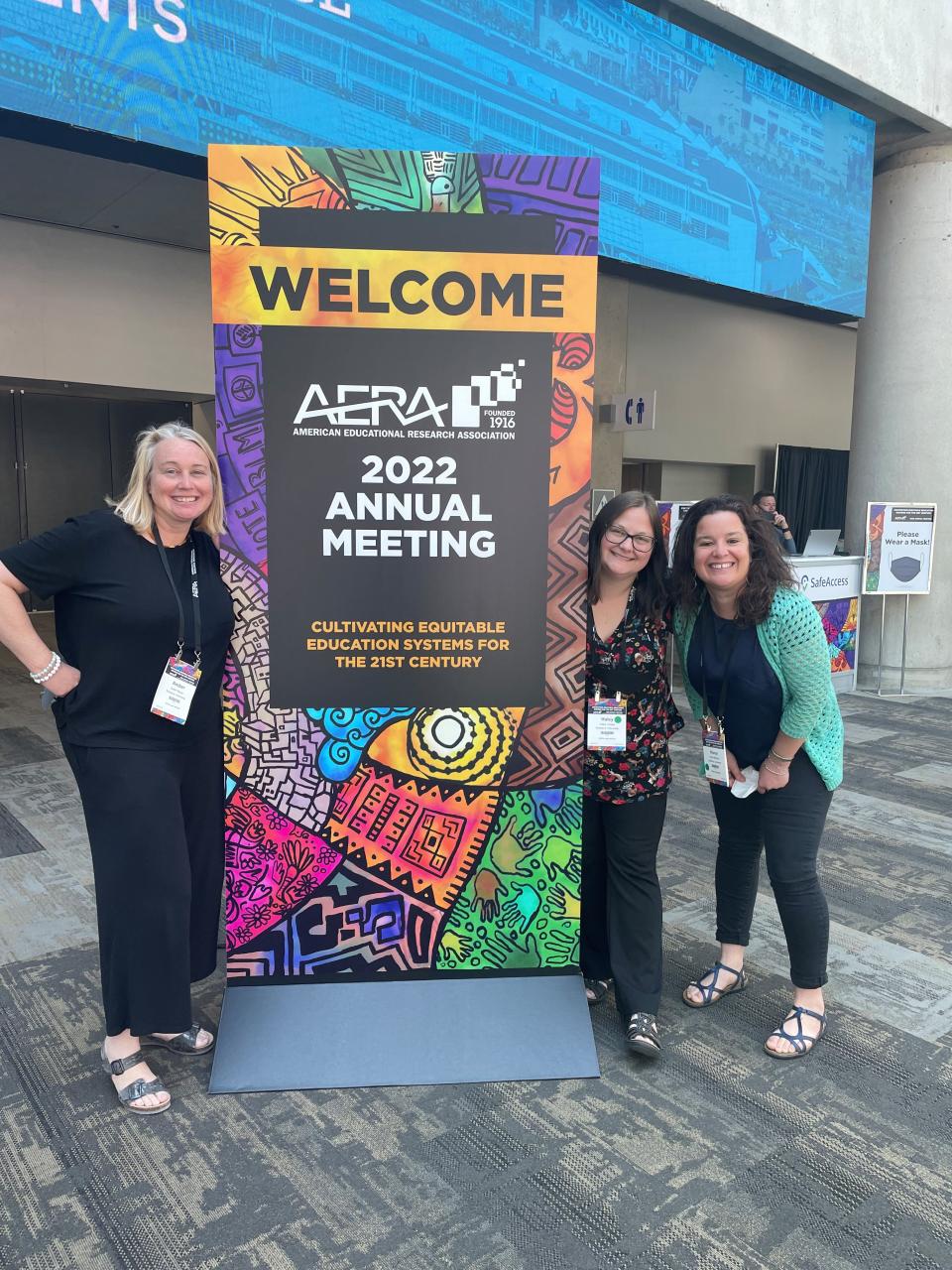 Dr. Amber Meyer and graduate students Haley Cristea and Honor McElroy stand beside an AERA 2022 Annual Meeting Welcome sign.