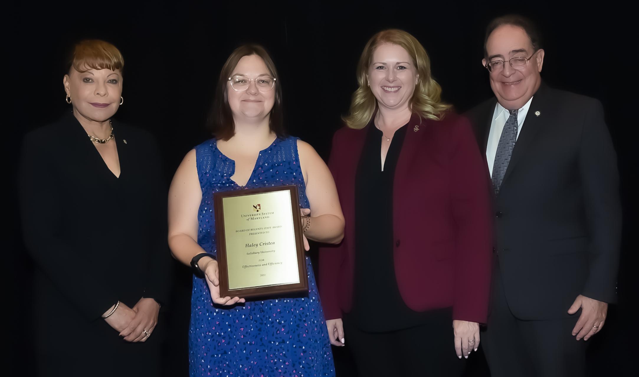 Haley Cristea holds a plaque award, flanked by SU President Lepre, Jay Perman, Chancellor of  the USM, and BOR Chair Linda Gooden 