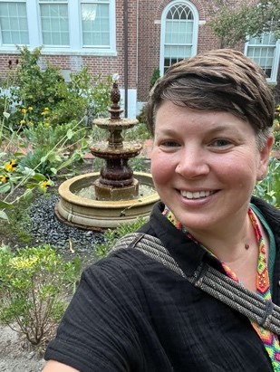 A selfie of Dr. Erin Stutelberg in front of the fountain in the rose garden outside of Holloway Hall.