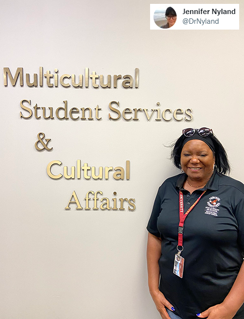Carolyn Frisby in front of the Multicultural Student Services & Cultural Affairs signage