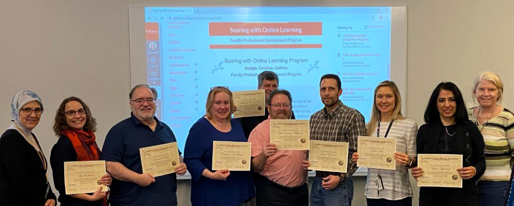 SU Faculty stand with completion certificates with the Soaring with Online Learning training course projected in the background.