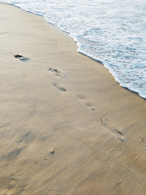 Picture of an imprinted footprint in the sand with a foamy ocean wave approaching