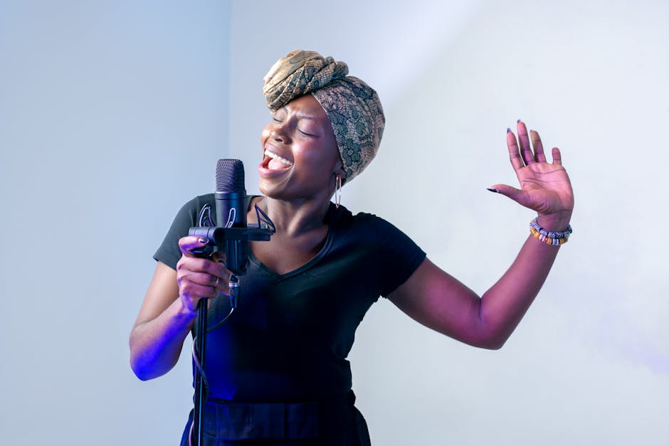 A black woman sings joyfully into a microphone with one hand up to stress emotionh