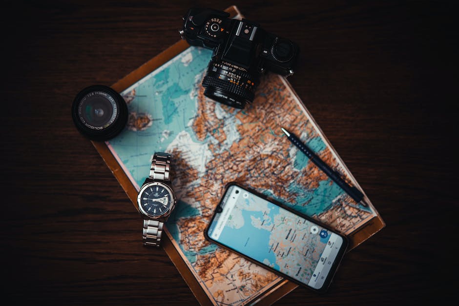 Camera, pen, cellphone, watch and compass on top of a map of Asia and top of Africa.
